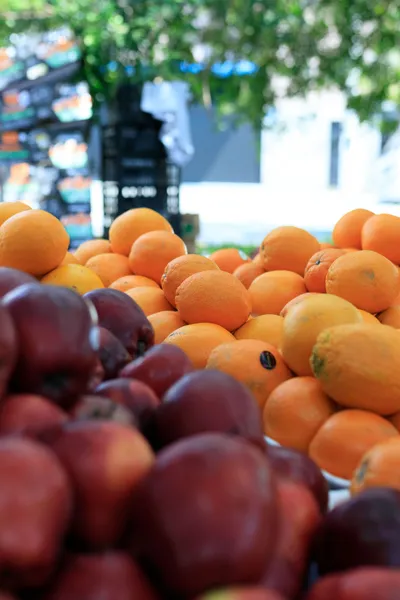 Display of fresh oranges and red apples at an outdoor market stand. 